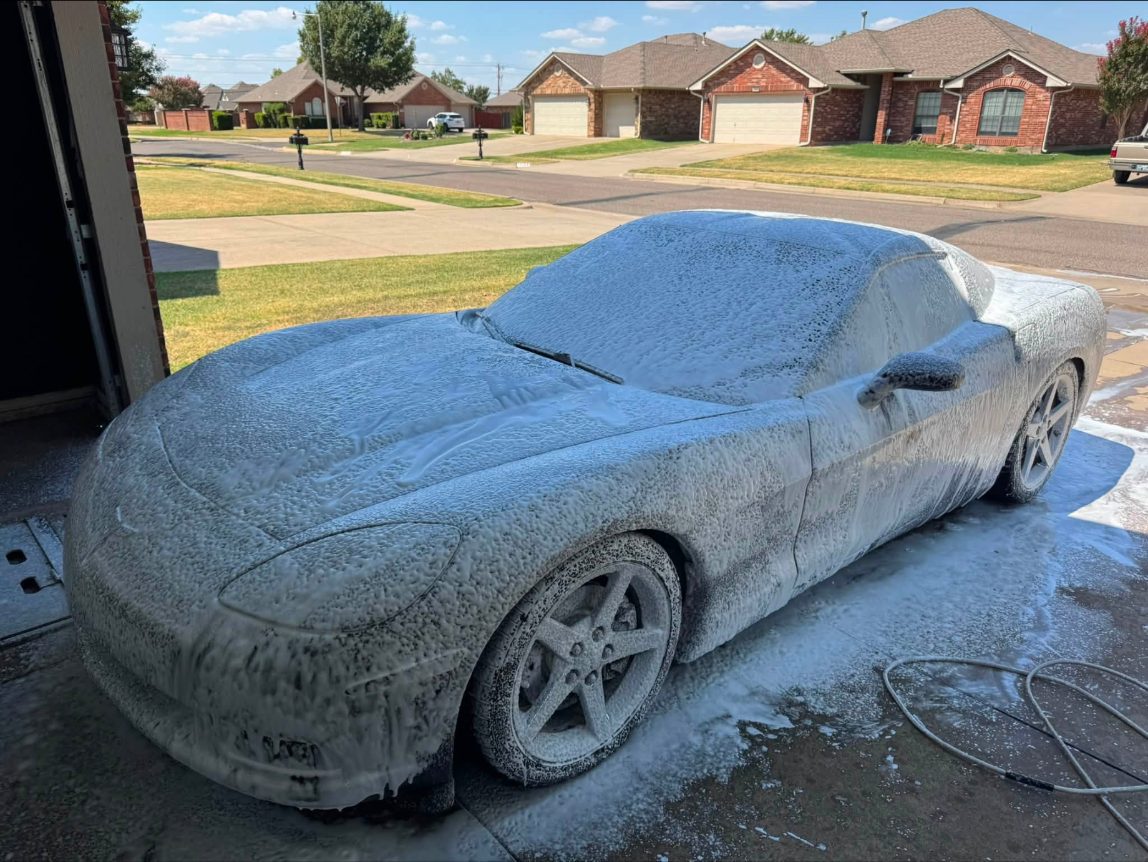 Black Corvette covered in thick foam pre-wash in the driveway